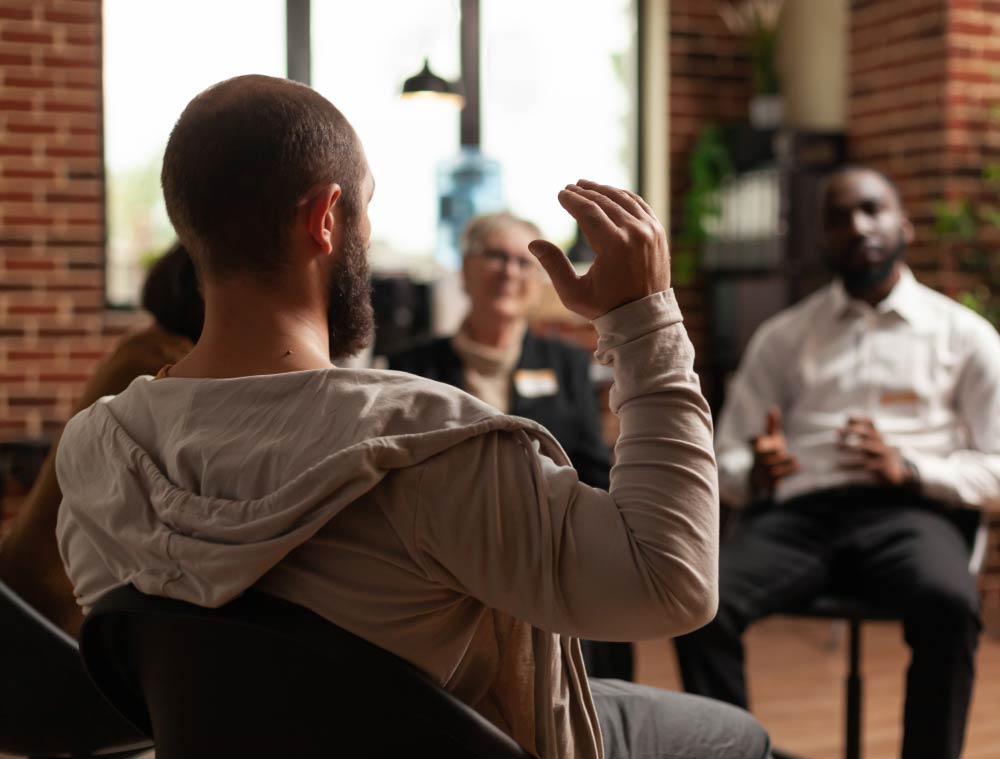 A man is sitting in a chair talking to a group of people.