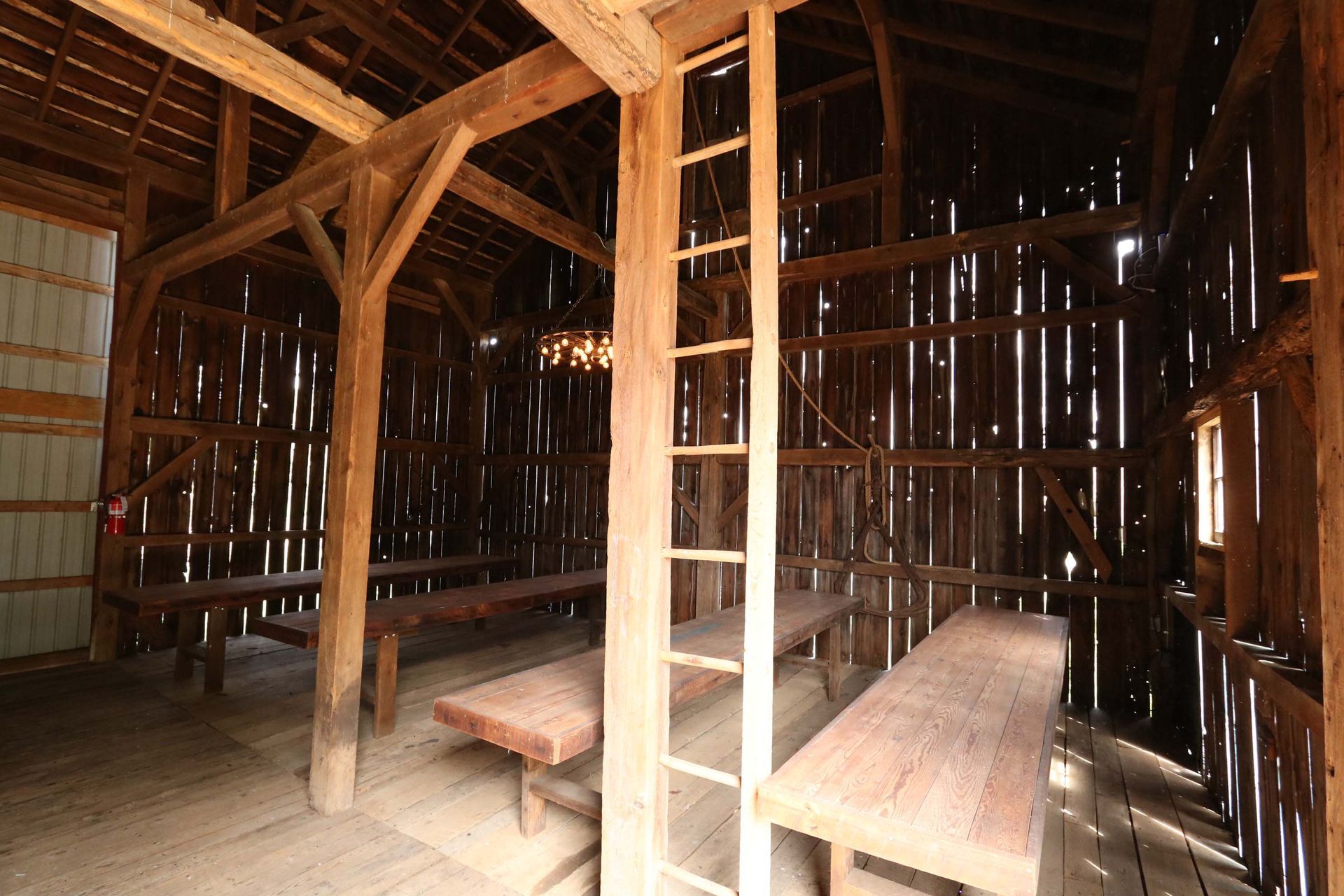 Inside of an aged wooden barn with long hand made barn wood tables and a ladder.