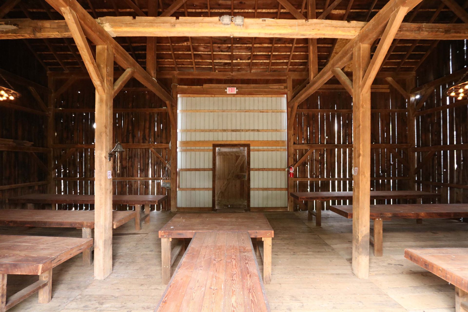 Interior of a barn with wooden tables and beams. A doorway is at the end, and the walls are made of wooden planks.