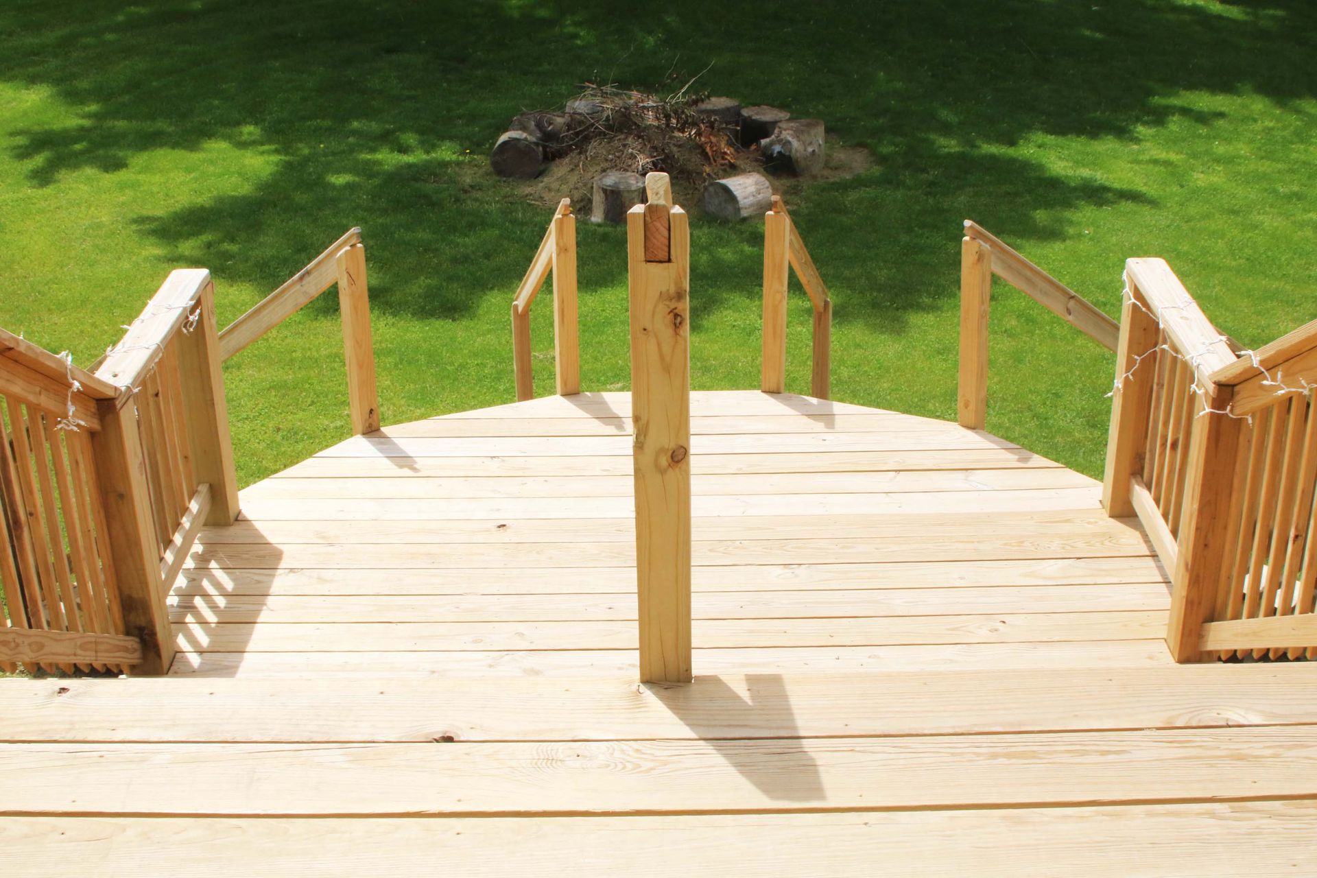Wooden deck with stairs leading to green lawn and fire pit..