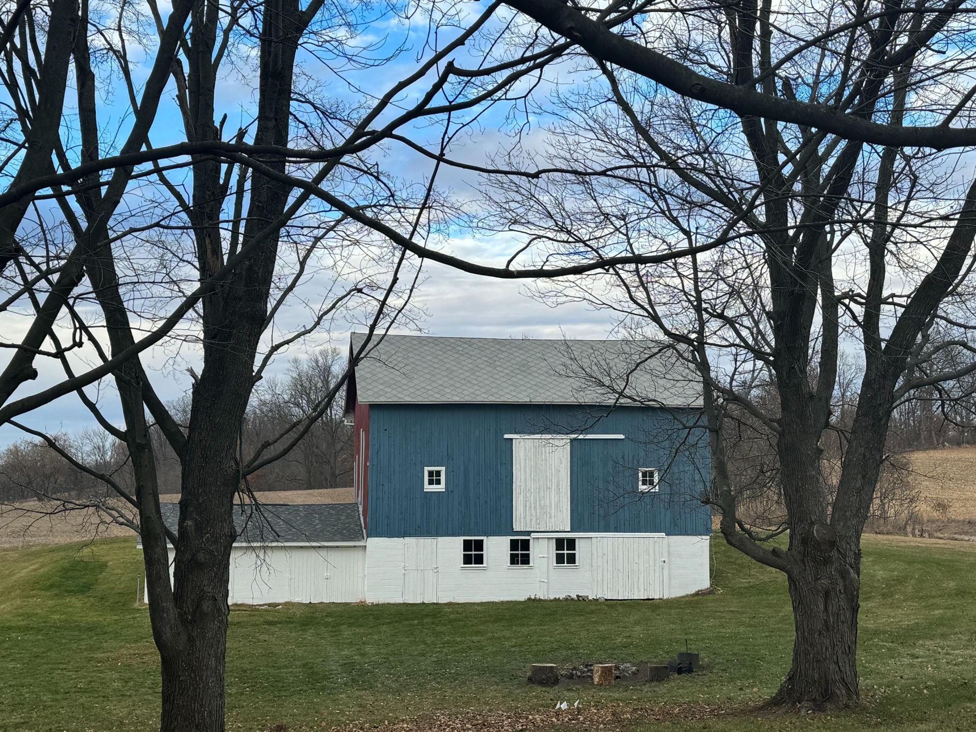 A blue and white barn is surrounded by trees in a field.