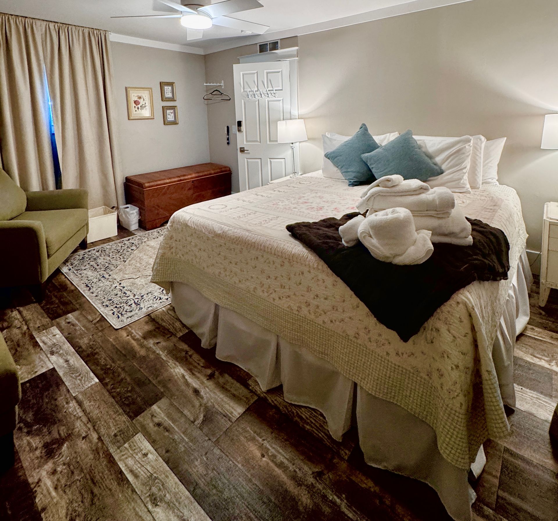 Bedroom with  king bed, chair, and chest, featuring wood-look flooring and beige walls.