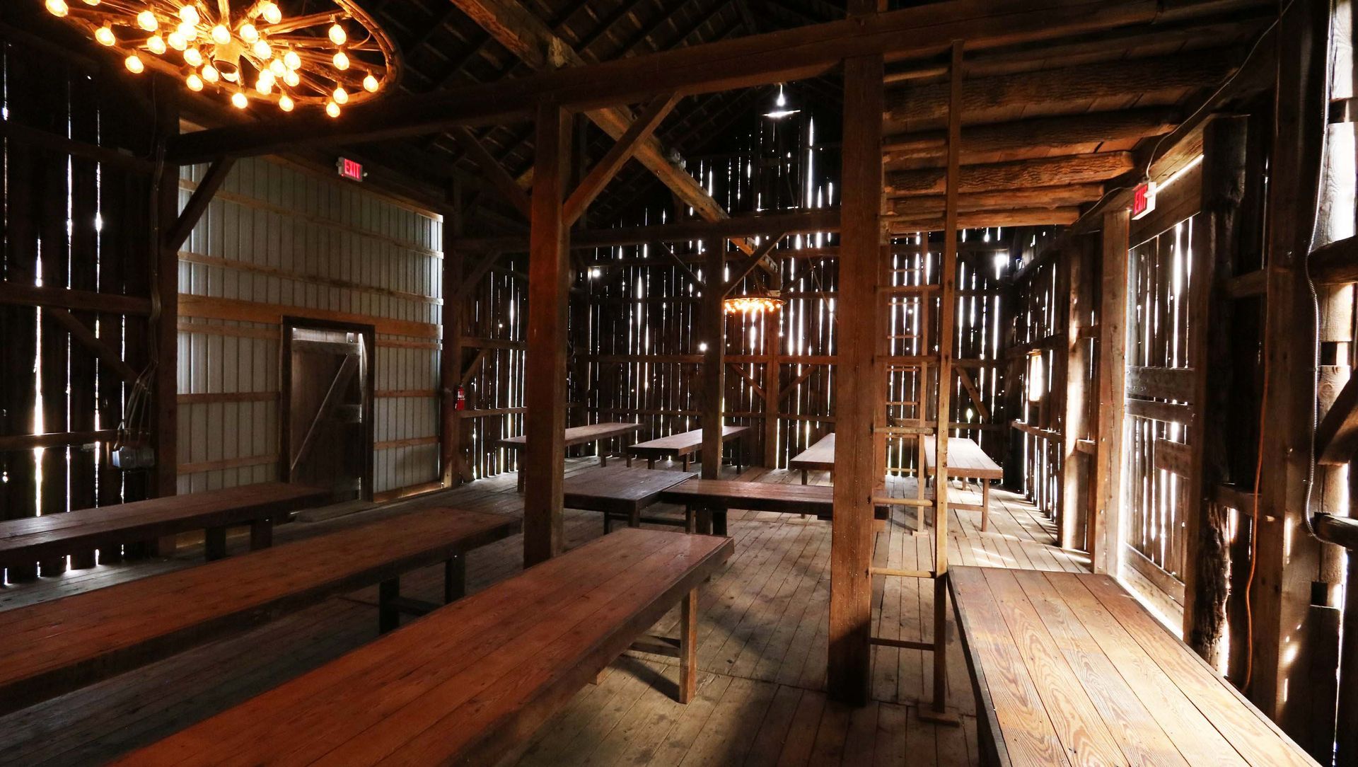 Inside a rustic barn with long wooden tables and string lights.