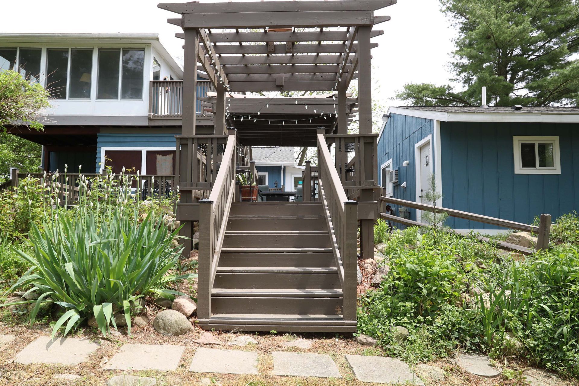 Wooden stairs leading up to a pergola, with buildings in the background and garden in the foreground.