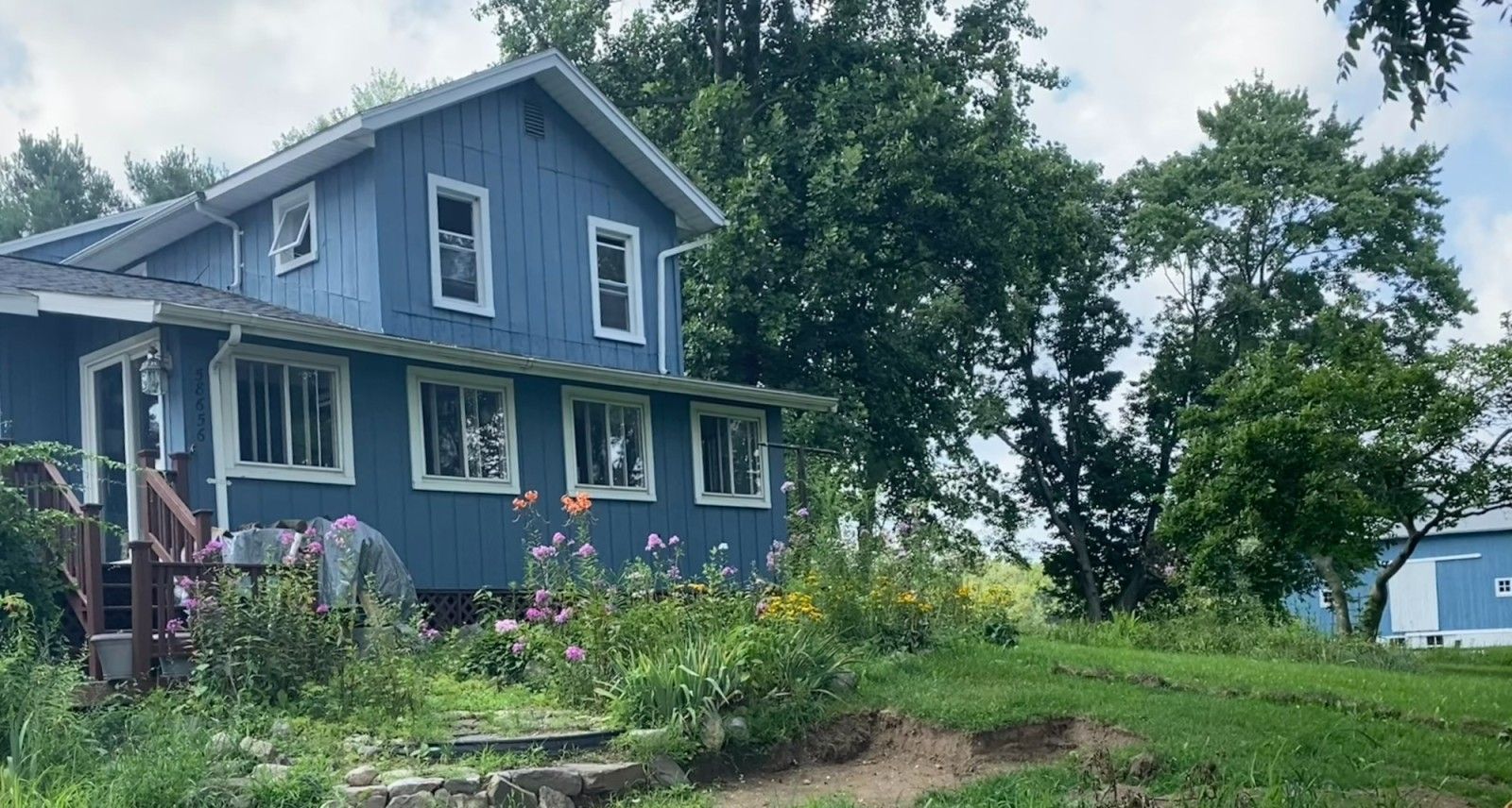 A blue house with a lot of windows is surrounded by trees and flowers.