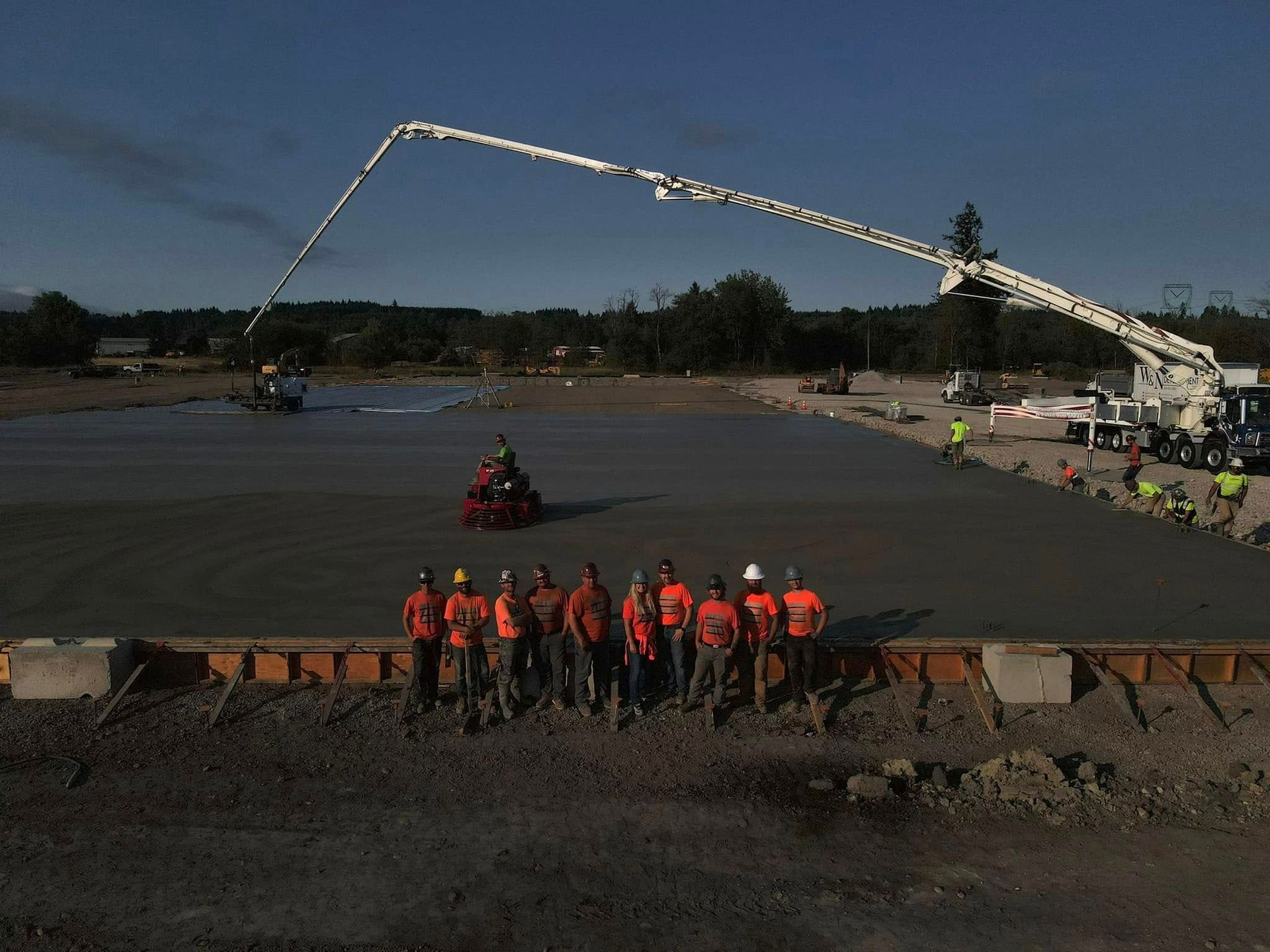 Workers in orange vests stand by a flooded area as a long crane extends overhead.