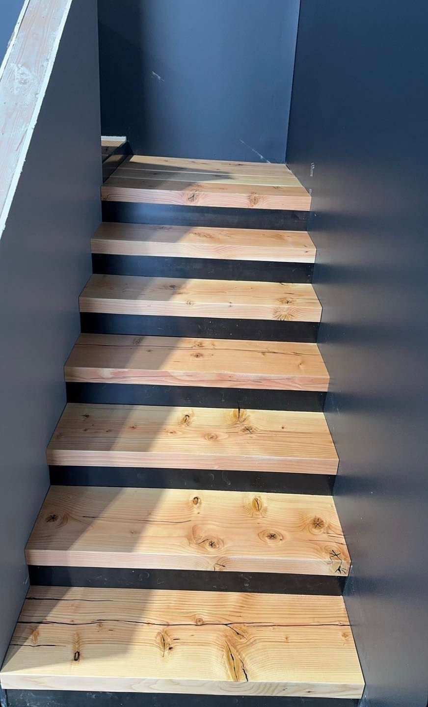 Wooden stairs with dark side walls in a narrow indoor stairwell.