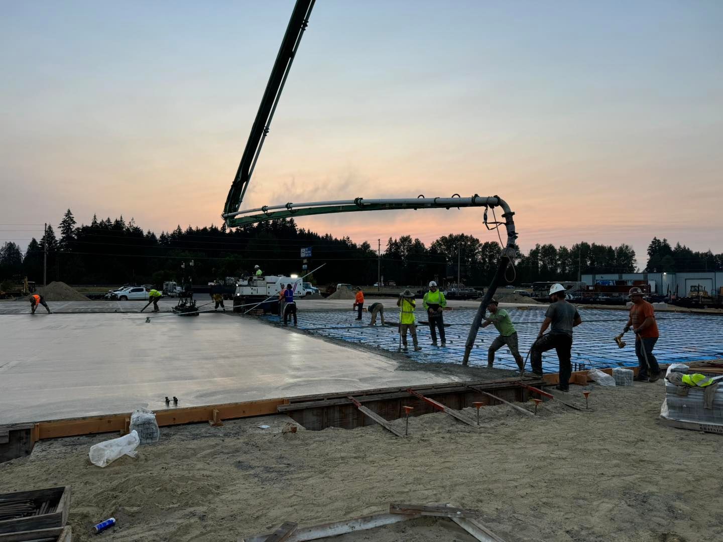 Workers pouring a concrete slab at dusk, with a boom pump and crew on a construction site.