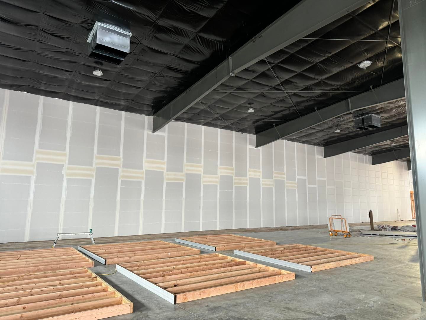 Empty construction interior with white walls, exposed black ceiling, and stacked lumber on the floor