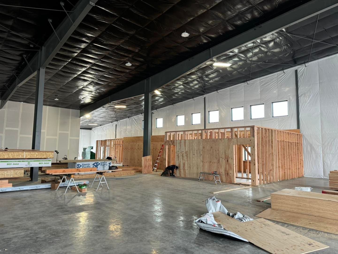 Large unfinished warehouse interior with exposed walls, high ceiling, construction materials, and scaffolding