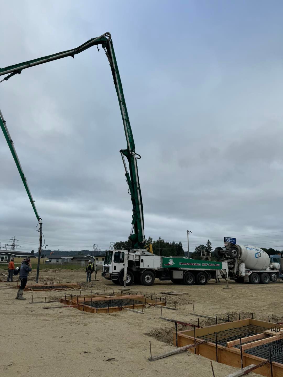 Concrete pump truck pouring at a construction site, with worker and overcast sky