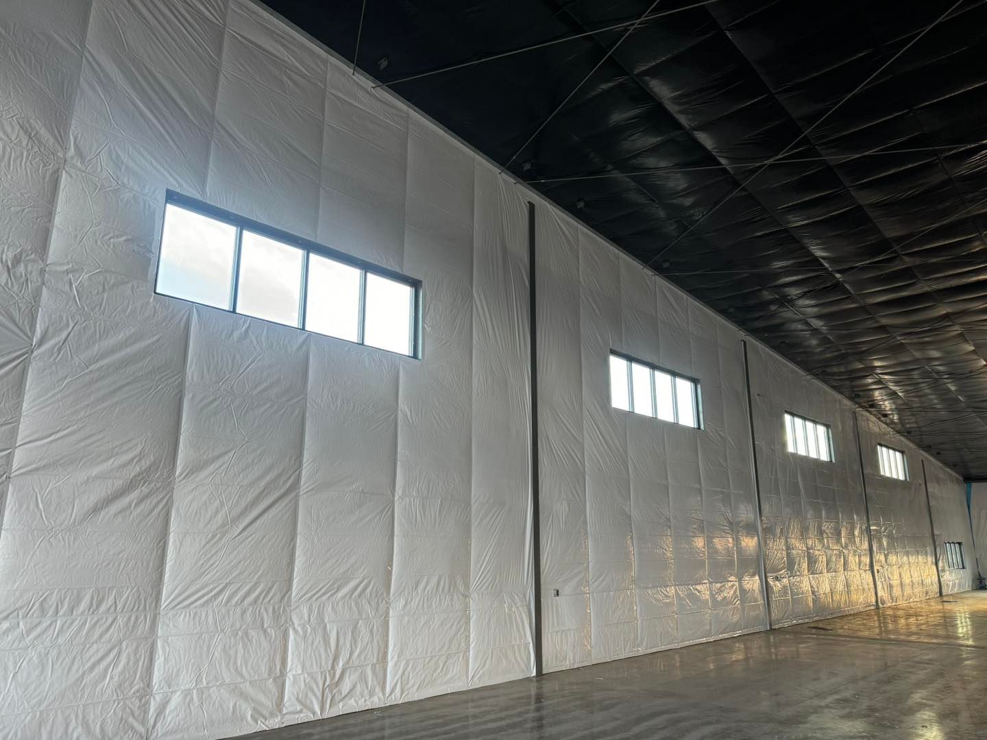Interior of a warehouse with insulated white walls, high windows, and a dark ceiling.