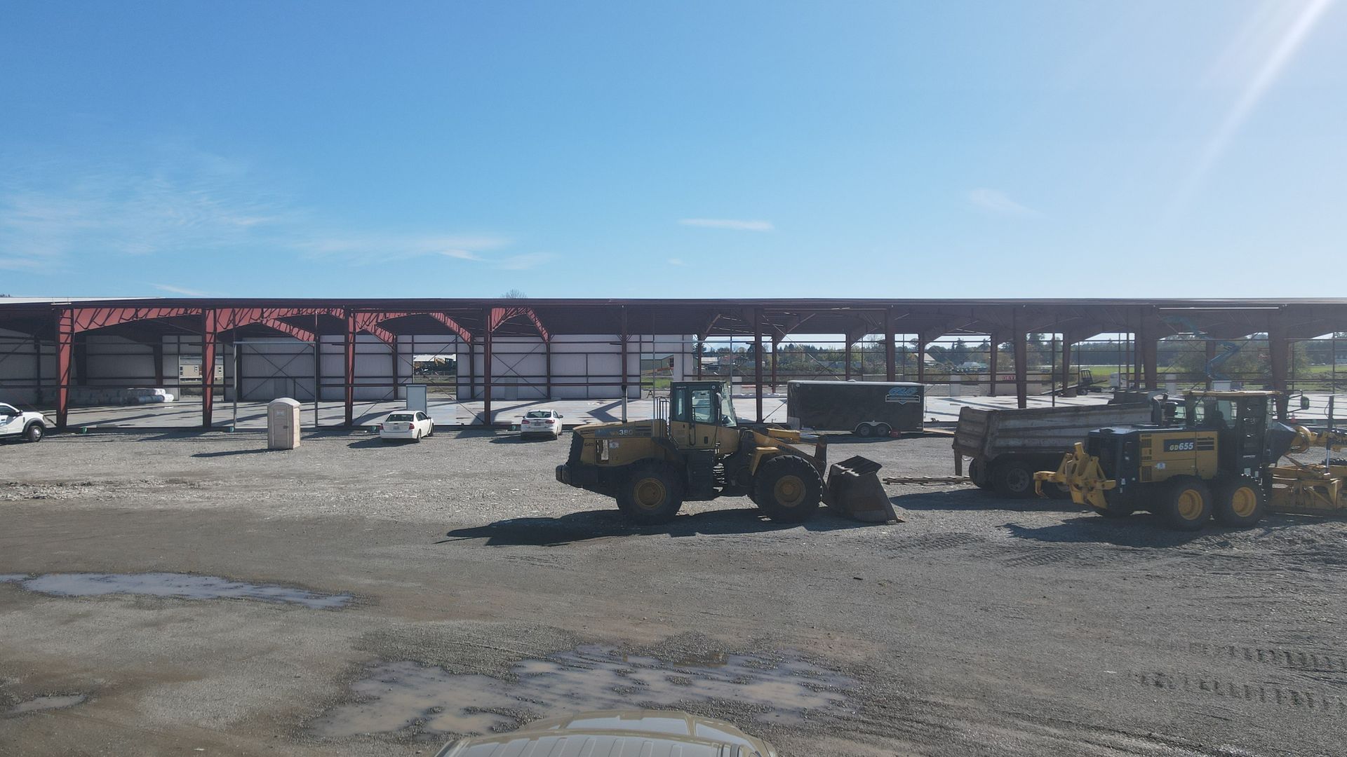 Construction site with two yellow bulldozers under a long open-sided shelter on a sunny day