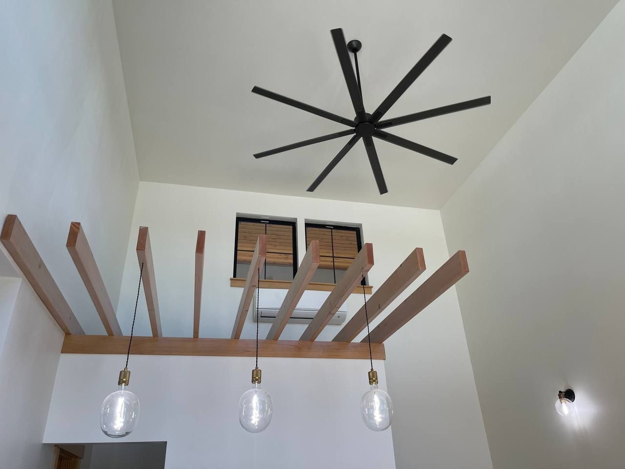High ceiling room with exposed wooden beams, hanging pendant lights, and a black ceiling fan