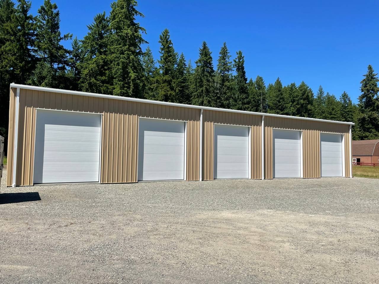 Row of beige storage units with white roll-up doors on a gravel lot under a blue sky