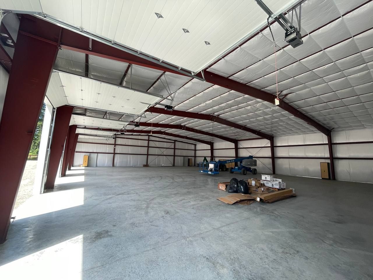 Large empty warehouse interior with white walls, red steel beams, and a concrete floor.