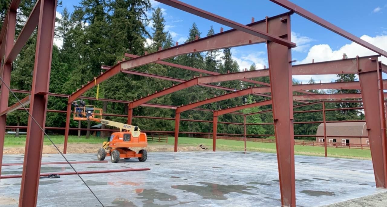Steel frame building under construction with an orange lift on a concrete slab outdoors.