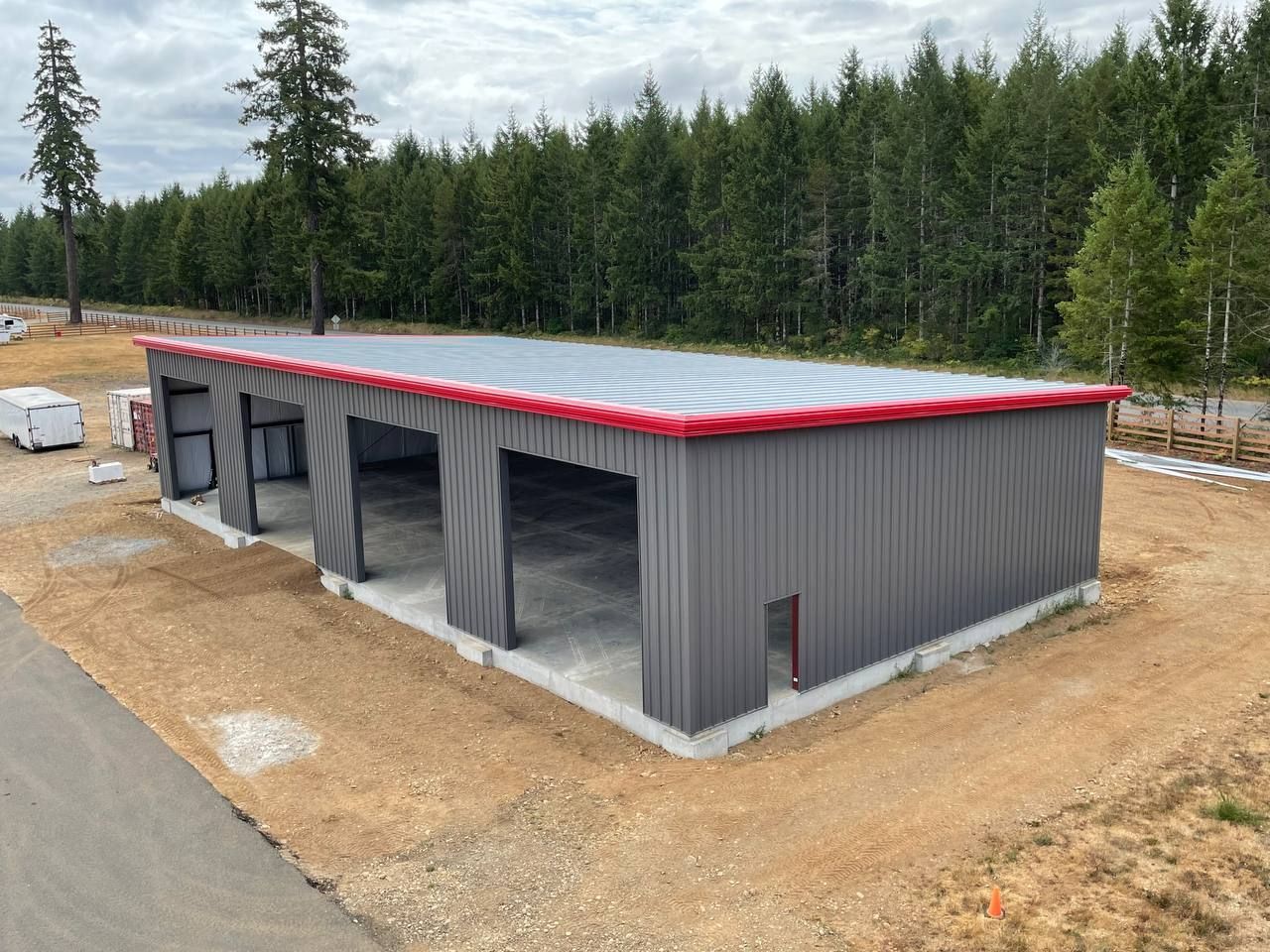 New gray metal building with red roof trim at a construction site surrounded by trees