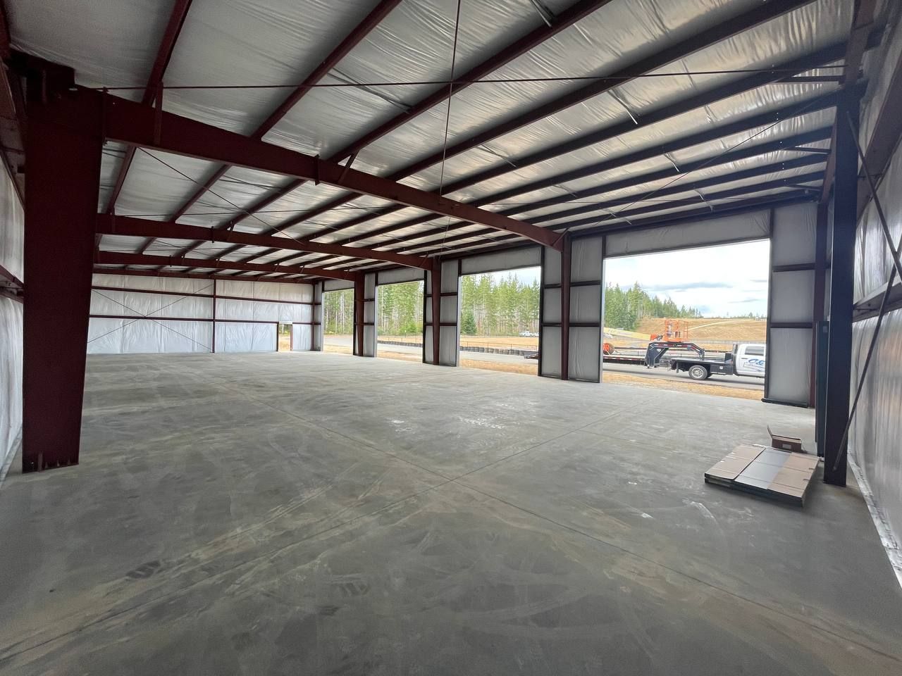 Empty steel-framed warehouse interior with concrete floor and large open bay doors
