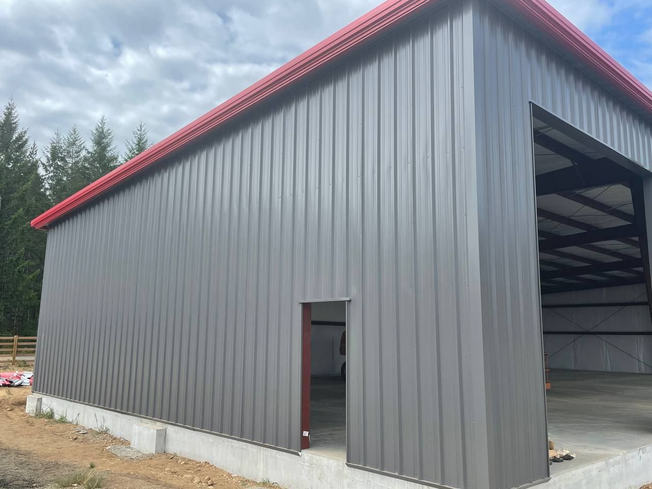 Gray metal warehouse with red roof trim, shown from the corner on a concrete foundation