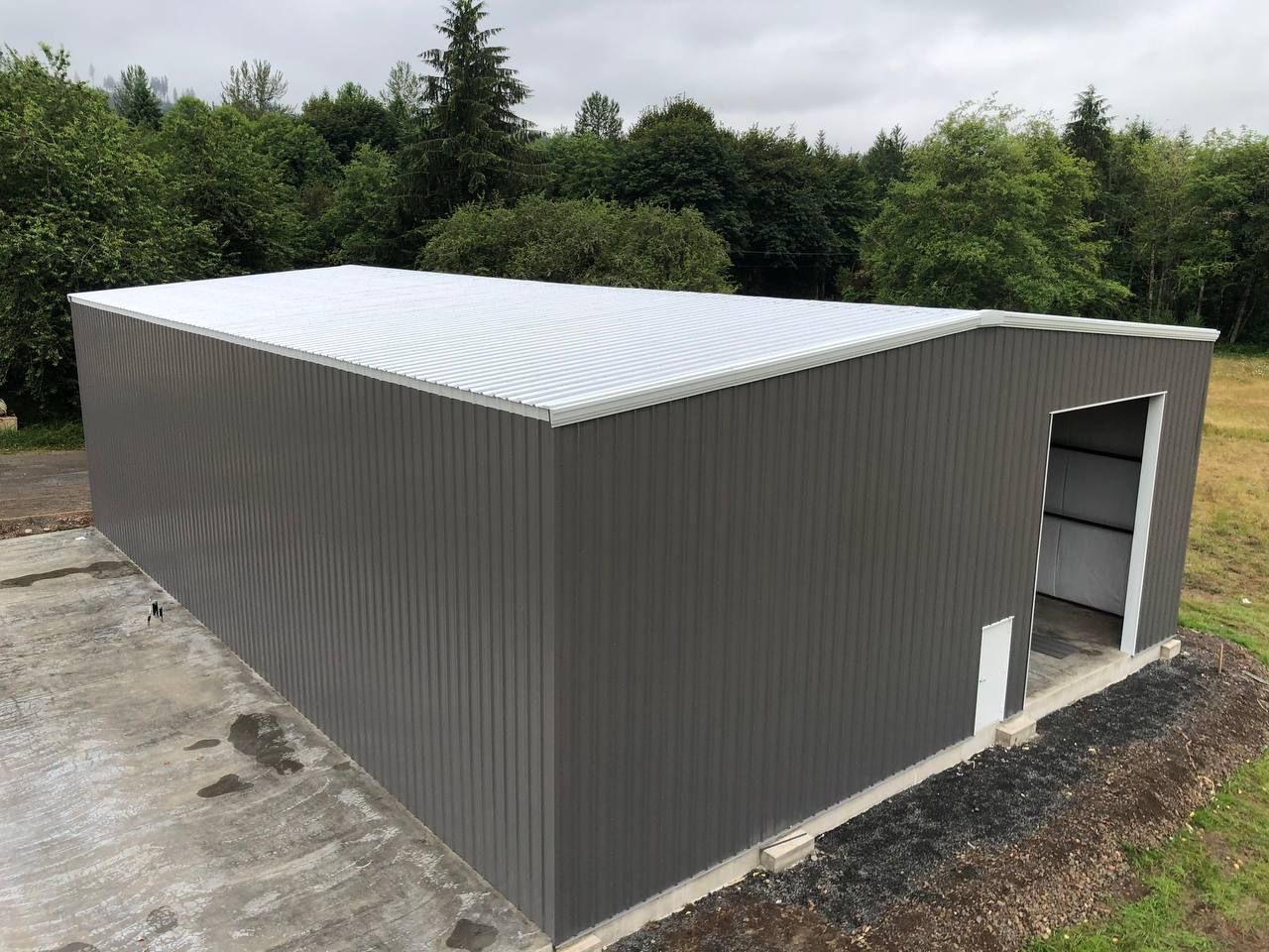 Gray corrugated metal storage shed with white roof, viewed outdoors near trees