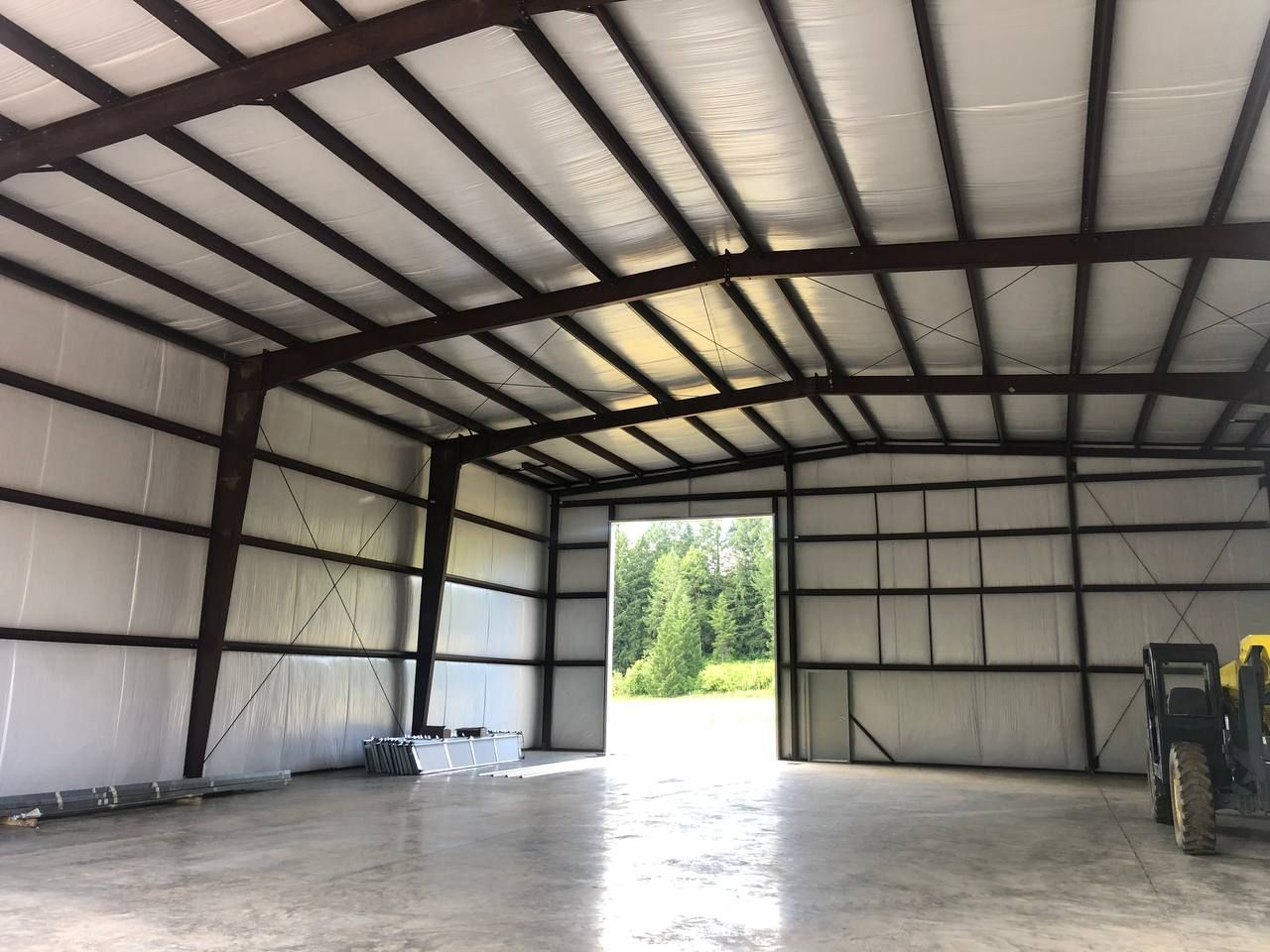 Interior of a metal warehouse with open doorway, white insulated walls, and a forklift on the right.
