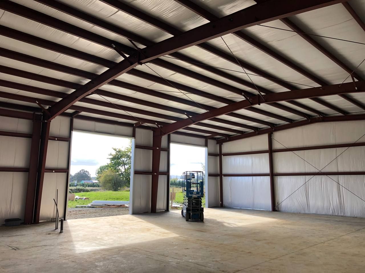 Empty warehouse interior with open roll-up doors and a forklift near the center.
