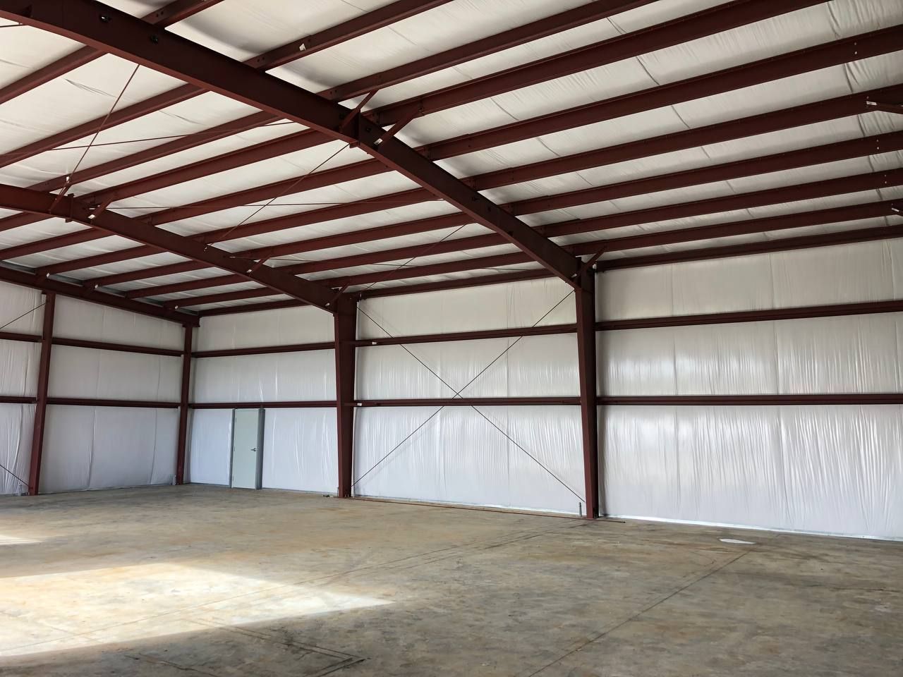 Empty metal warehouse interior with red steel beams and a concrete floor