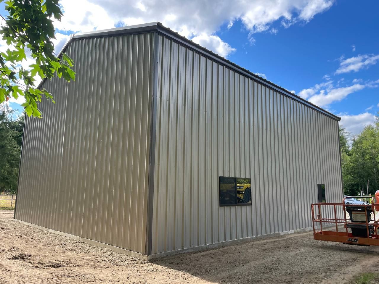 Large gray metal-sided shed with a small window, shown outdoors under a blue sky