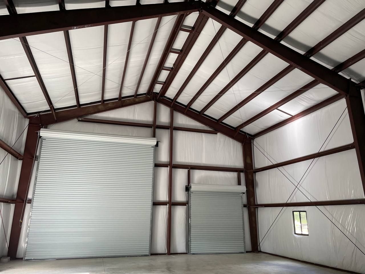 Interior of a metal warehouse with two closed roll-up doors and a small window on the right.