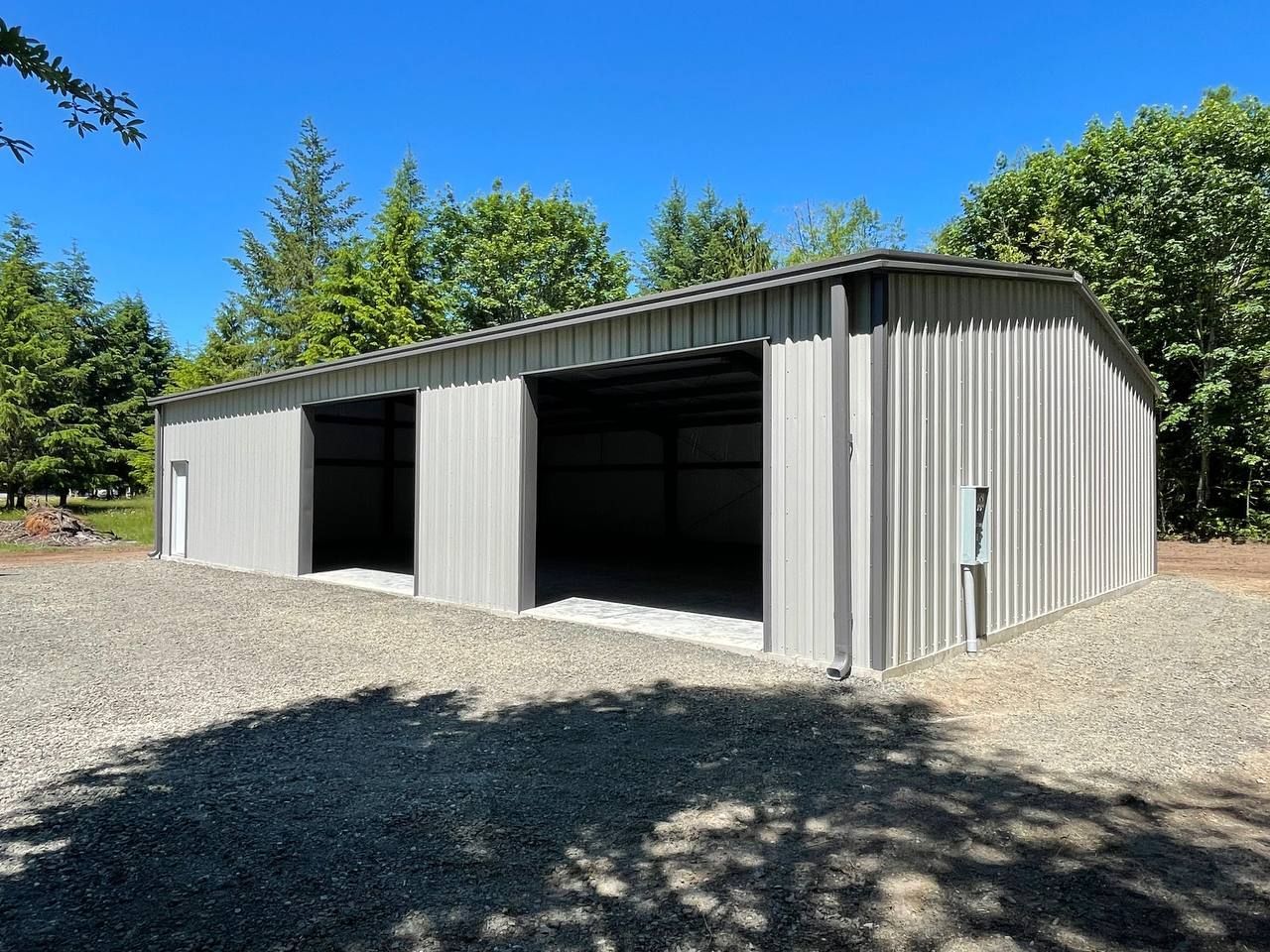 Gray metal storage building with open bays on a gravel lot under a blue sky