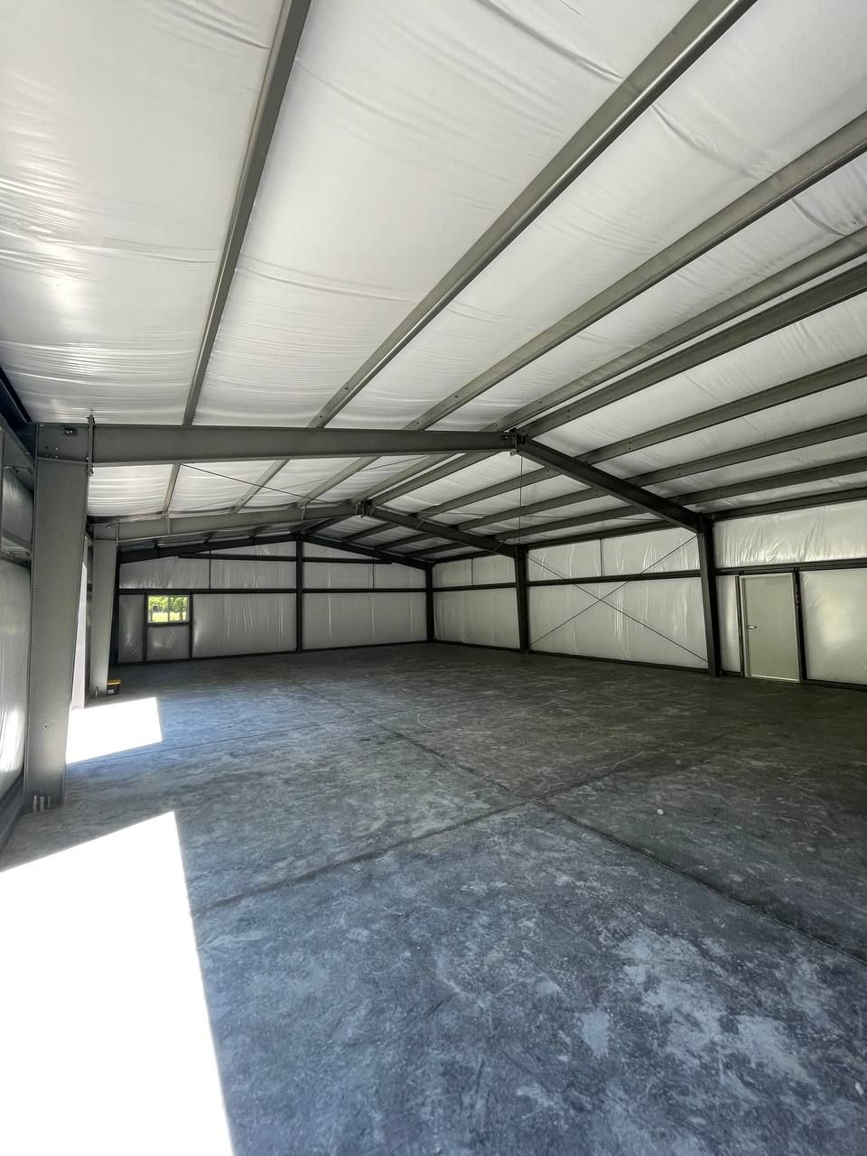 Empty metal-framed warehouse interior with concrete floor and bright light from the open side