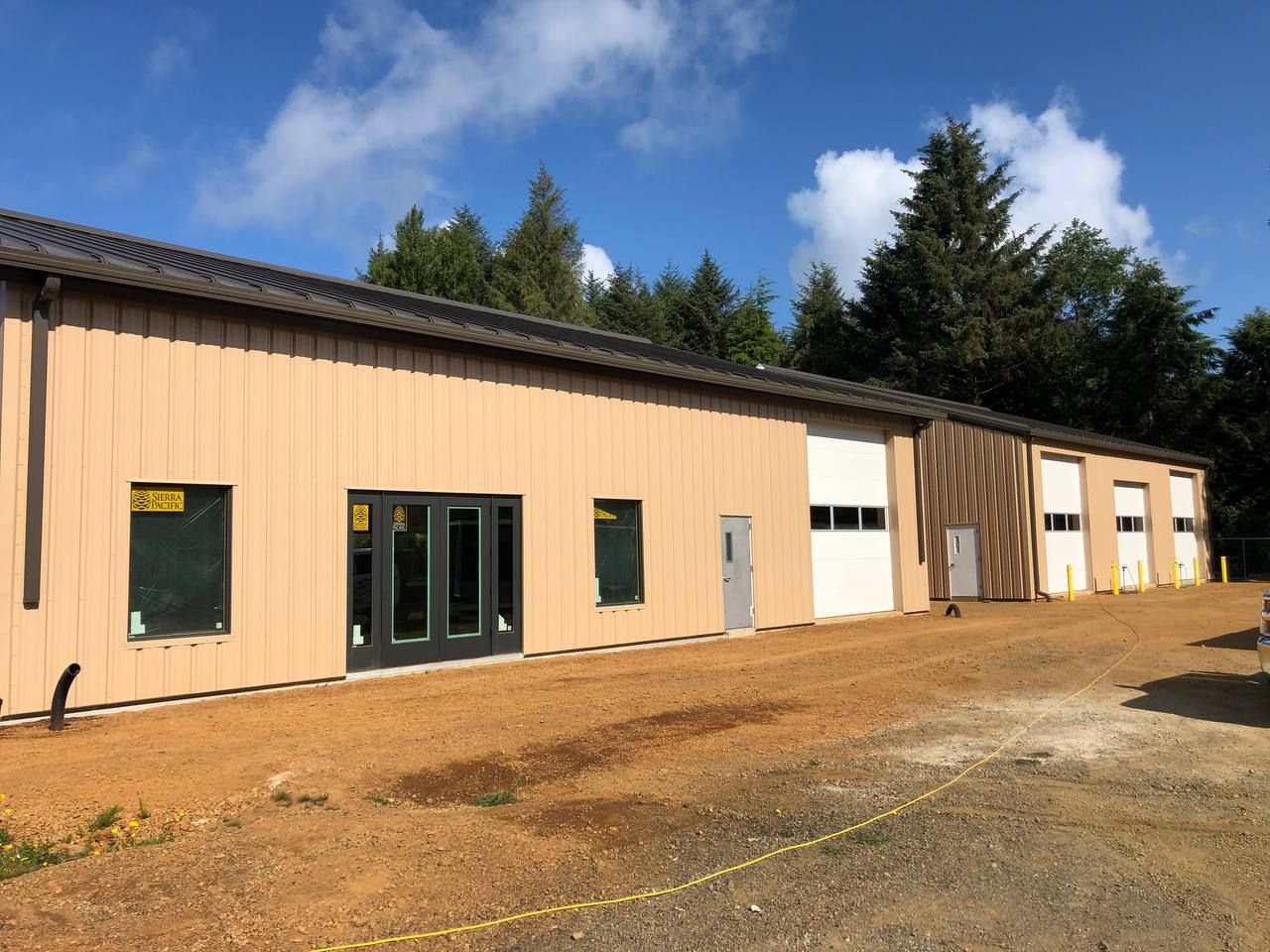 Long tan industrial building with multiple garage doors on a gravel lot under a blue sky