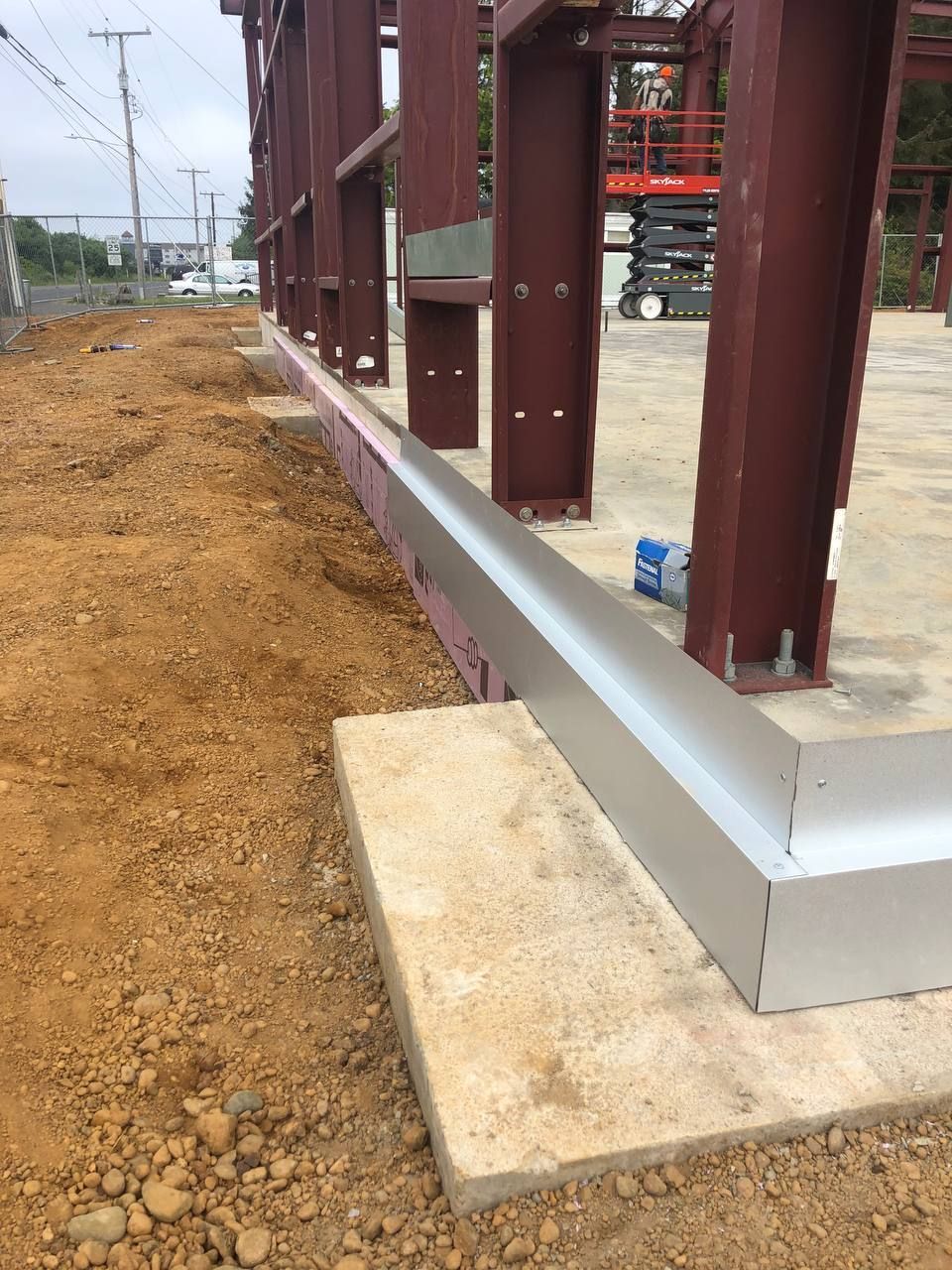 Steel building frame on concrete foundation beside a dirt construction site.