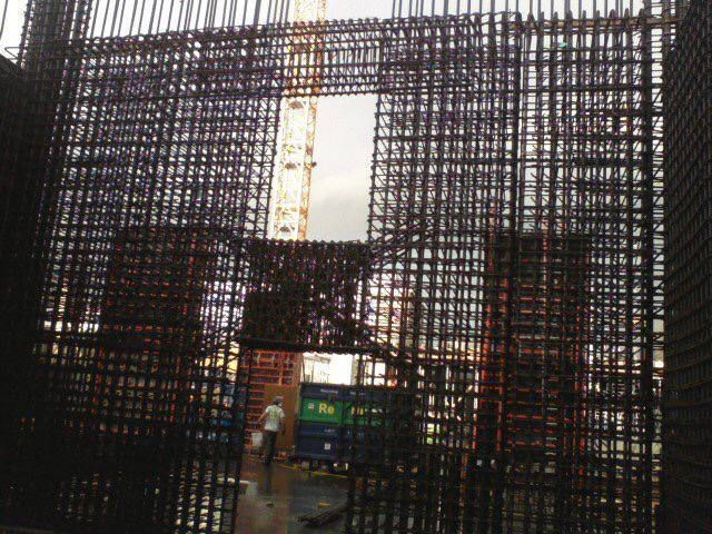 Construction site viewed through dark mesh netting, with a crane and a blue truck in the background
