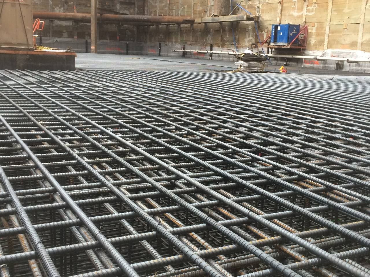 Steel rebar grid covering a concrete construction site floor with brick walls in the background