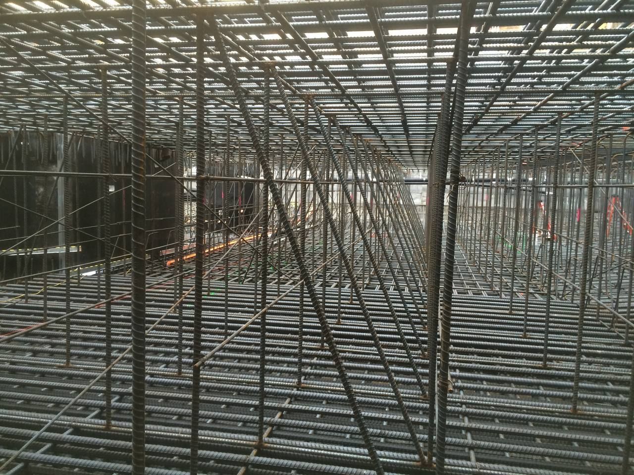 Steel rebar framework inside a construction site, with a large scaffolding grid overhead