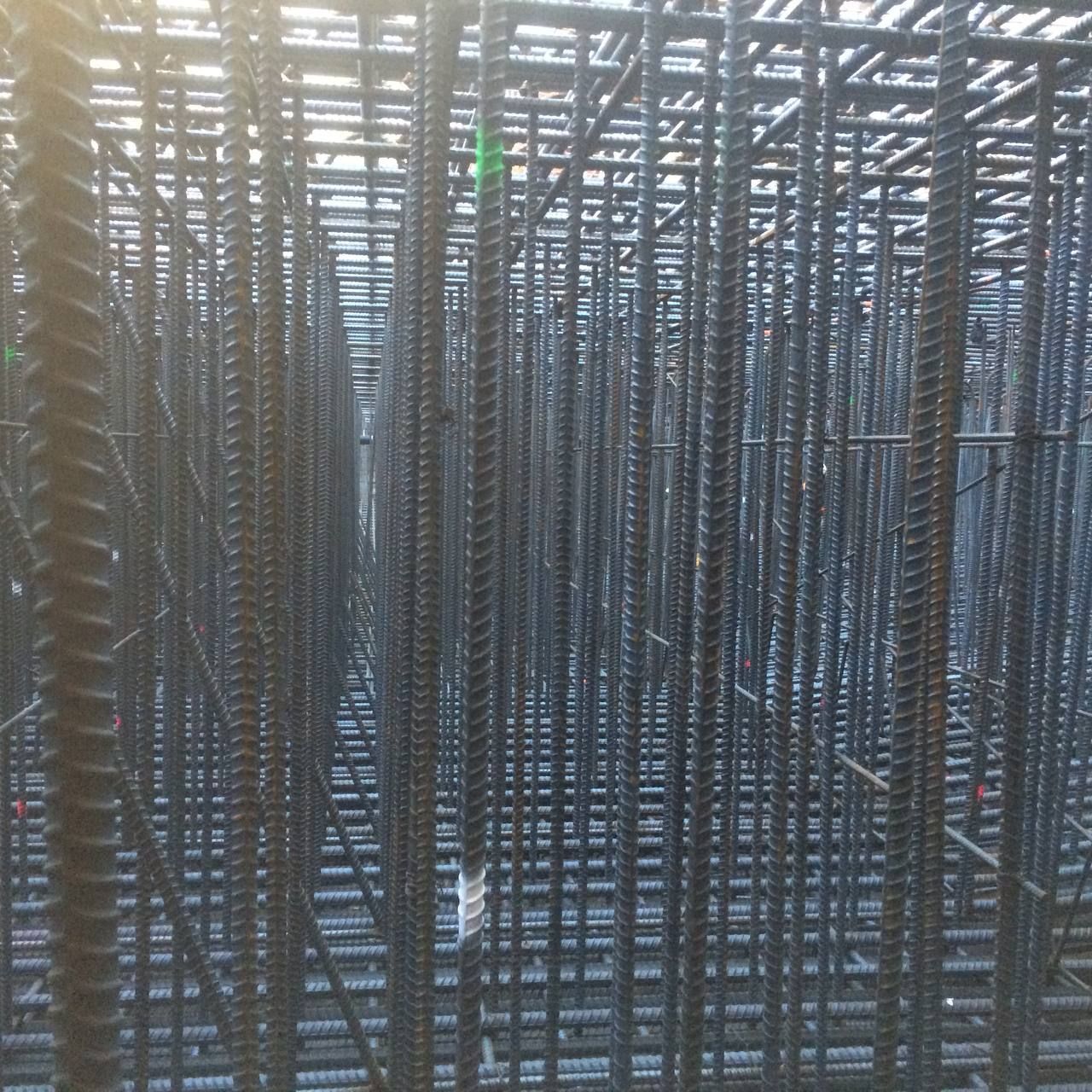 Dense grid of vertical steel rods and horizontal beams at a construction site, forming a repeating pattern