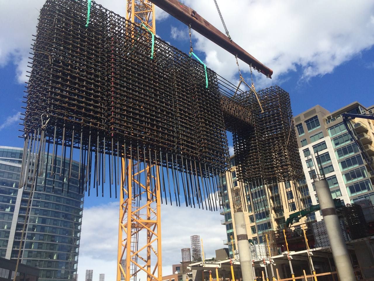 Construction site with crane lifting steel rebar panel beside modern buildings under a blue sky