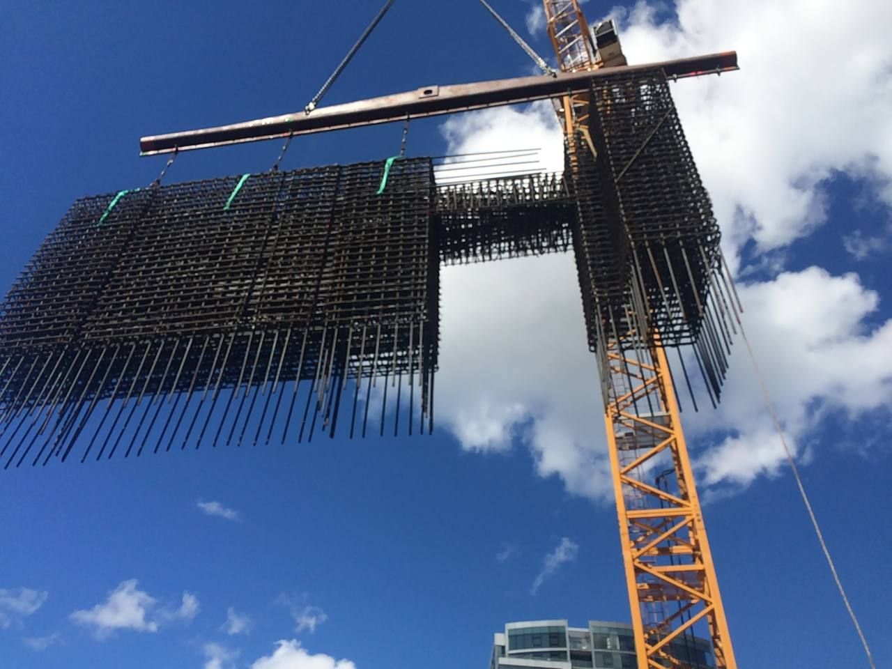 Construction crane lifting a large black metal mesh panel against a blue sky