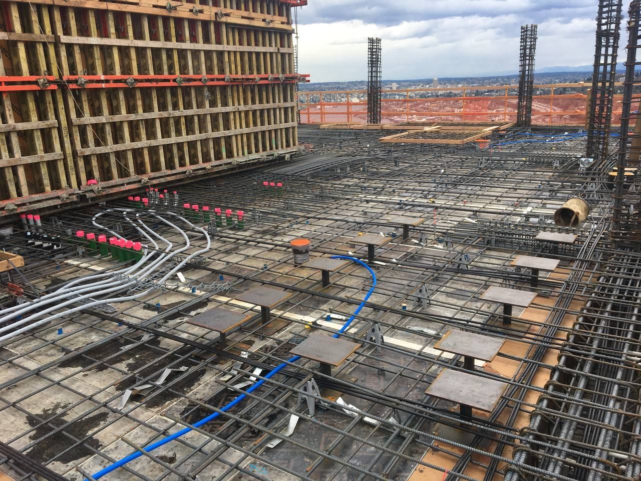 Construction site with rebar grid, blue conduit, and formwork for a concrete foundation slab.