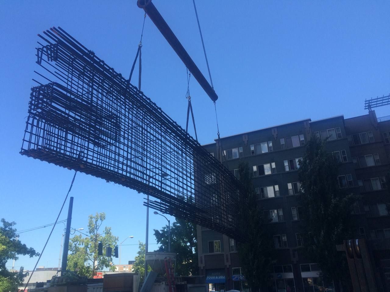 Construction crane lifting a large steel rebar frame beside a building under a blue sky