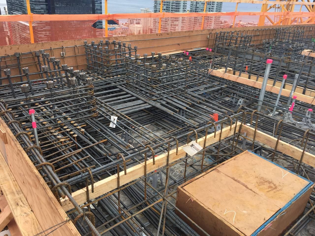 Rebar grid and wooden formwork for a concrete foundation under construction, with orange safety barriers.