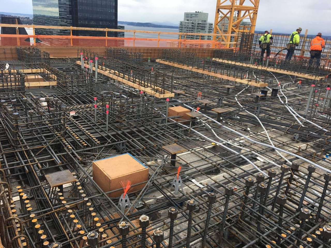 Construction site with rebar foundation grid, workers in hard hats, and a crane in the background