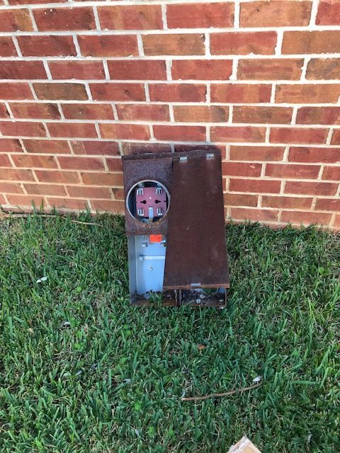 A brick wall with a meter sitting in the grass next to it.
