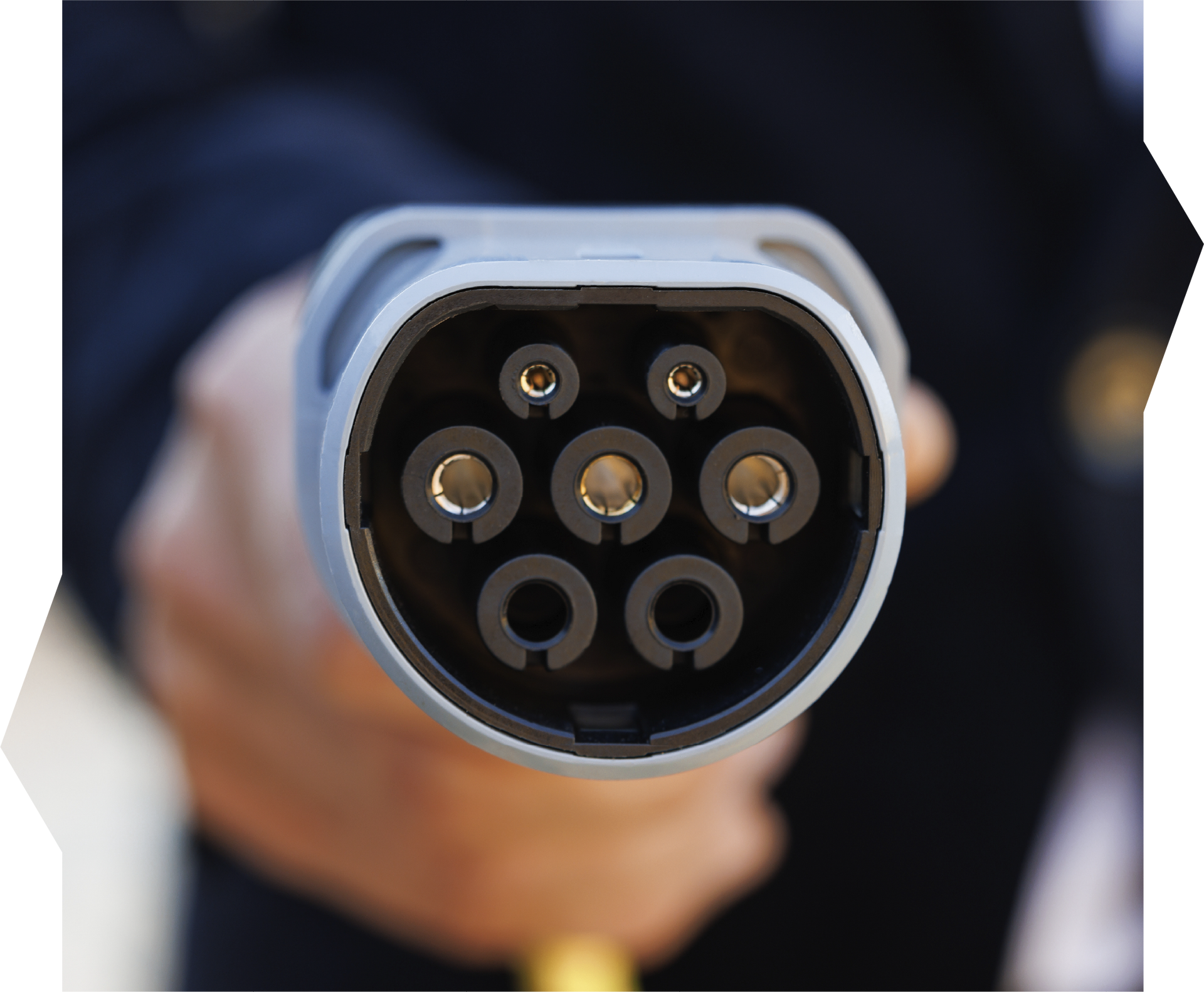 Close-up of a person holding a gray EV charging connector. Six circular holes are visible, with yellow cable in the background.