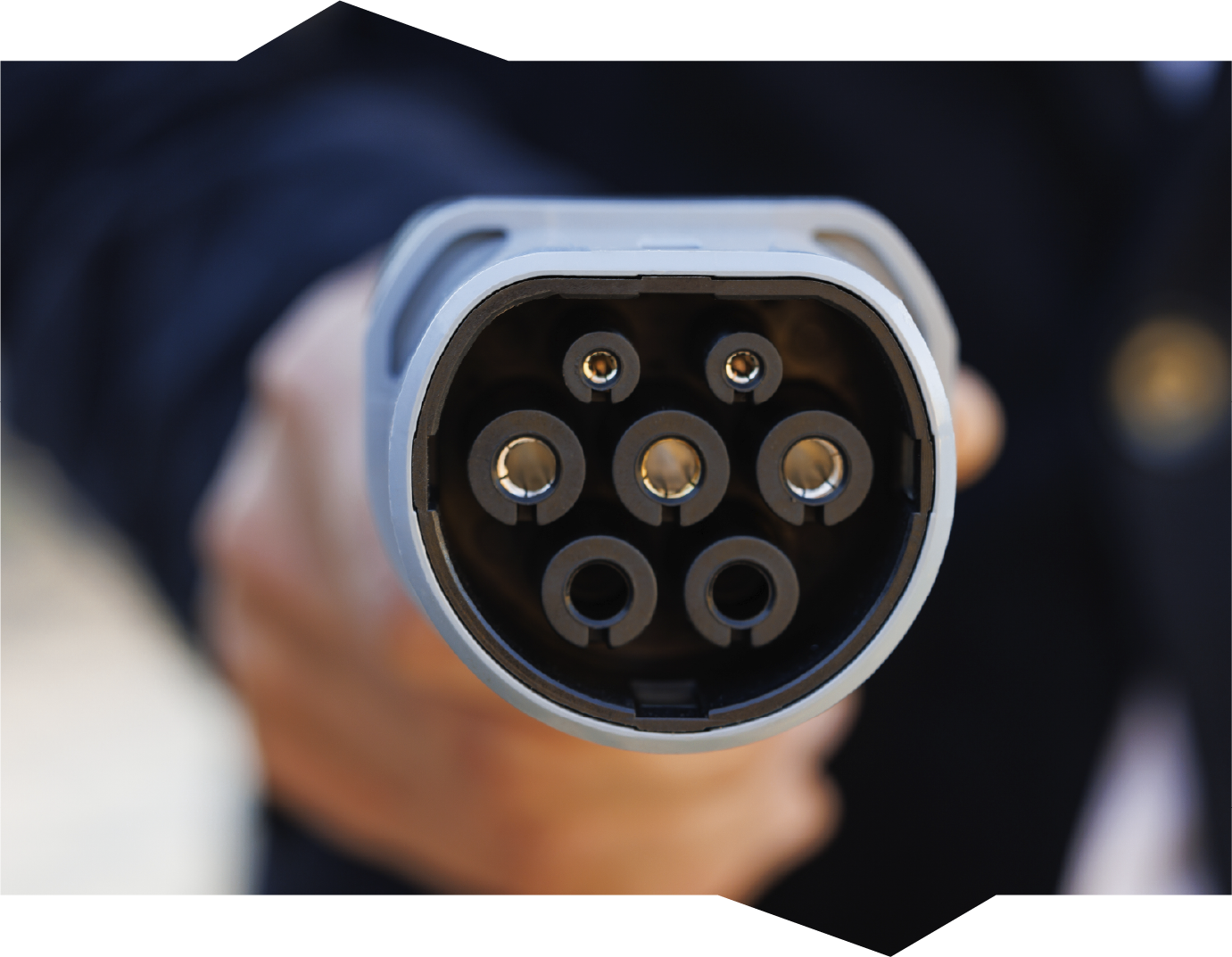 Close-up of a hand holding a gray EV charging connector with multiple pin holes.