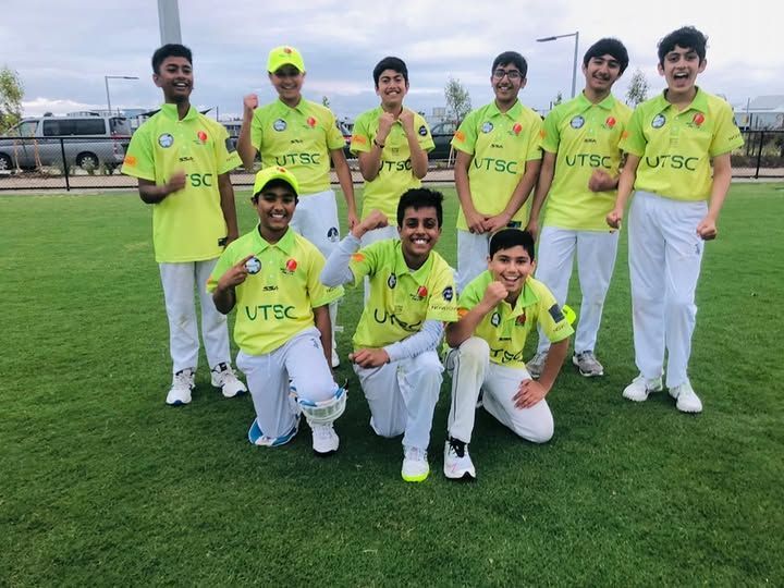 A group of ten cricket players in matching lime-green jerseys and white pants stand on a field, smiling for a team photo.