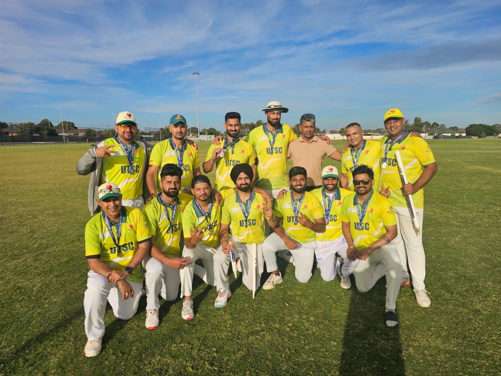 A cricket team in bright yellow jerseys and white pants poses for a group photo on a sunny field.