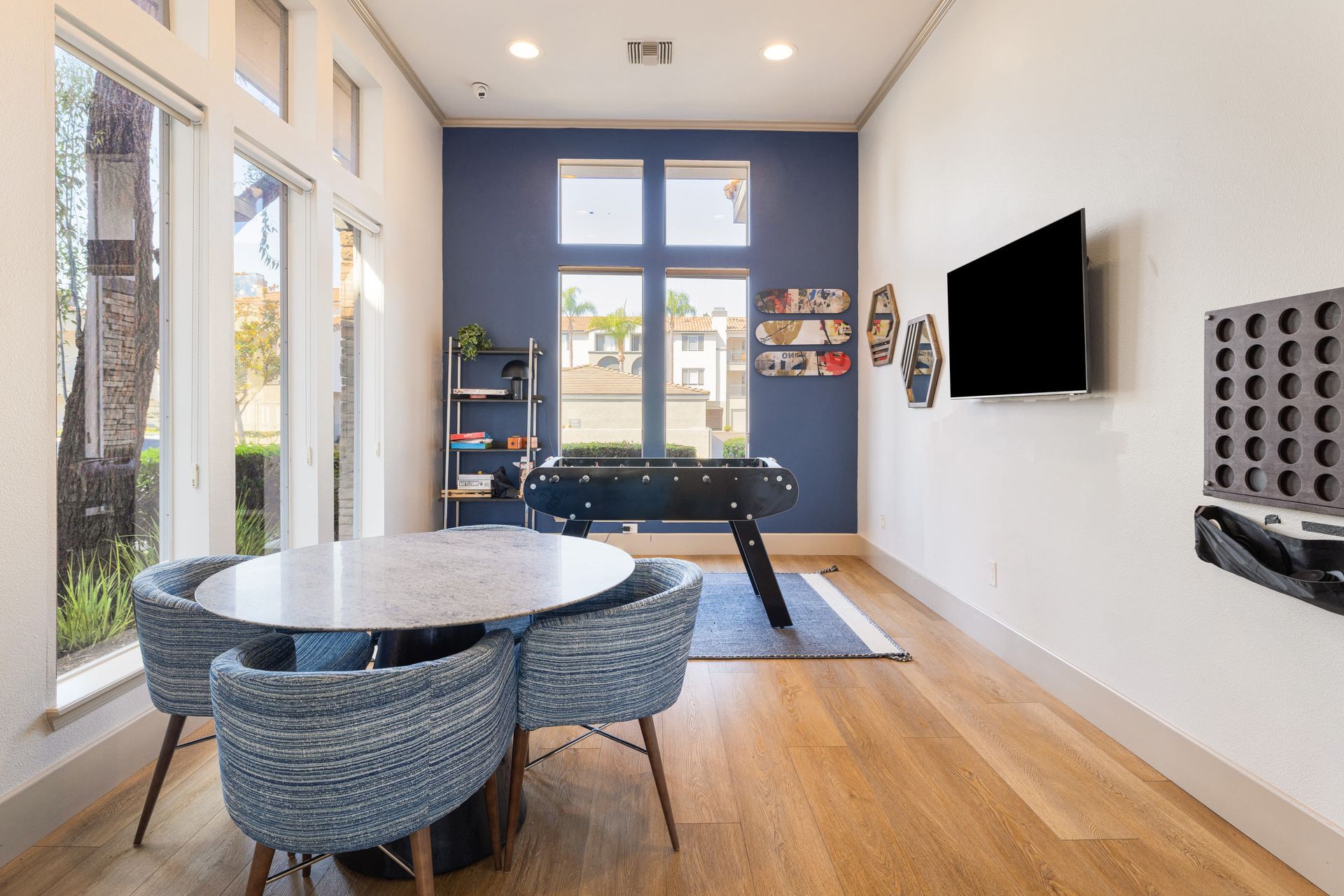 Bright communal lounge with a foosball table, round marble table, and large windows at Alize Apartment Homes in Aliso Viejo, CA.